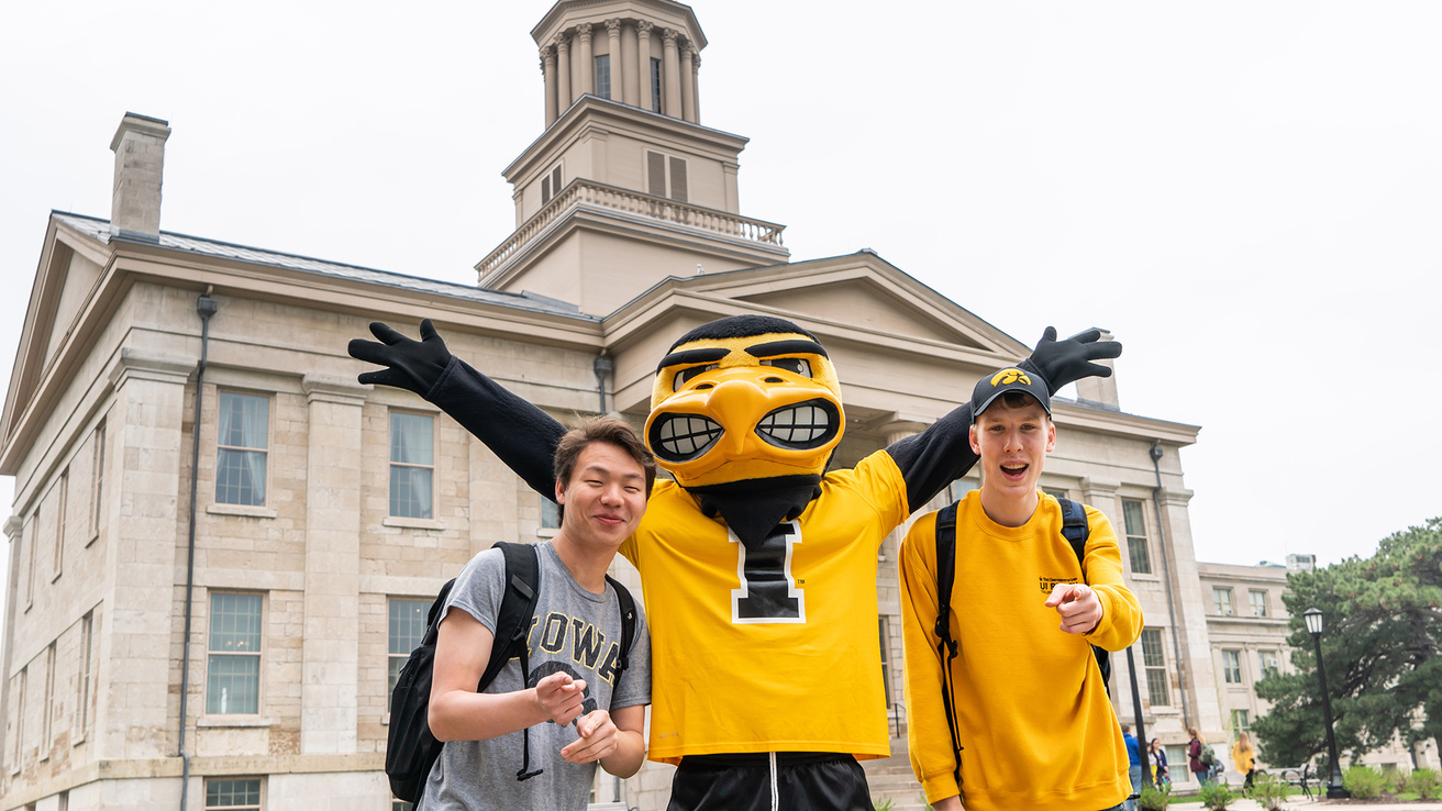 Herky with two male students in front of Old Capitol