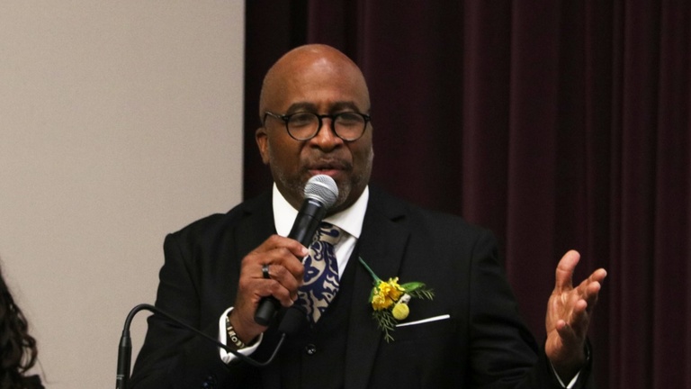 Bill Lloyd stands at a podium, delivering a speech at the 2026 UI REACH graduation.